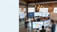 Modern business team collaborating in industrial office space with data analytics dashboards and interactive displays for strategic planning.