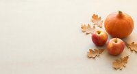 Autumn harvest composition with orange pumpkin, red apples and golden oak leaves on neutral background for seasonal decorating and fall celebrations.