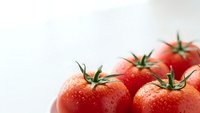 Fresh ripe red tomatoes with water droplets on white background for healthy cooking and organic food preparation.