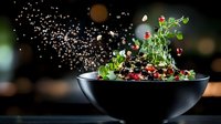 Fresh salad with quinoa, microgreens and pomegranate seeds tossed in black bowl against dark background with water splash and bokeh effect.