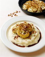 Roasted cauliflower steak on creamy mashed potatoes with toasted almonds and herb garnish, served with sauce reduction for gourmet dining.