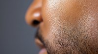 Close-up profile of African American man's face showing detailed skin texture and facial hair stubble against neutral background for grooming concepts.