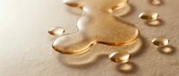 Golden oil droplets and liquid serum on beige surface, skincare and cosmetic ingredient for beauty, wellness, and dermatology applications.