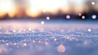 Sparkling snow surface with blurred bokeh lights and warm sunset glow creating magical winter atmosphere, macro close-up view of crystalline frost texture.