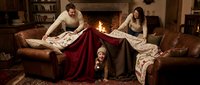 Family building blanket fort in cozy living room with fireplace. Mother, father and young daughter creating indoor tent for fun bonding activity at home.