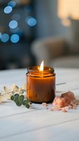 Amber glass candle burning with eucalyptus branch and healing crystals on marble surface creating cozy spa atmosphere with soft bokeh lights.