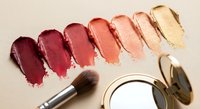 Lipstick color swatches in warm tones from deep burgundy to golden nude with makeup brush and compact mirror on neutral background for beauty tutorials.