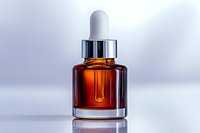 Amber glass dropper bottle with silver cap on reflective surface against light background, containing essential oil or serum for cosmetic and wellness products.