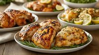 Grilled chicken thighs with herbs and citrus garnish served on white plates, featuring golden-brown crispy skin and charred edges, arranged for food photography.