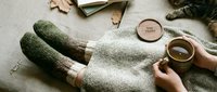 Cozy autumn scene with knitted socks, warm tea cup, sleeping cat, and stay home wooden coaster on soft blanket, top view.