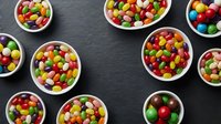 Colorful assorted candy in white bowls on dark slate background. Sweet treats for parties, celebrations, and confectionery displays.