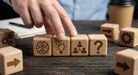 Business professional arranging wooden blocks with innovation symbols including brain, lightbulb, teamwork and question mark on office desk.
