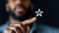 Young African American man holding glowing star shape, symbolizing achievement, dreams, and success against dark background. Focus on illuminated star and hand.