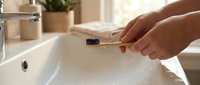 Woman holding bamboo toothbrush over white bathroom sink in modern eco-friendly morning routine for sustainable oral hygiene and zero waste lifestyle.