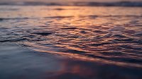 Gentle ocean waves at sunset with warm golden and purple hues reflecting on water surface creating peaceful seascape atmosphere for relaxation and meditation content.