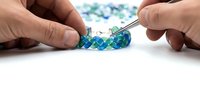 Hands crafting colorful blue and green beaded jewelry with pliers on white background. Handmade accessories creation process for DIY projects and crafting.