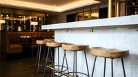 Luxury bar counter with white marble top and wooden stools in modern lounge setting with warm ambient lighting and dark wood cabinetry for hospitality design projects.