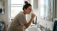 Young woman brushing teeth in modern bathroom mirror reflection morning routine dental hygiene care smiling happy healthy lifestyle wellness.