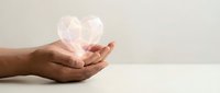 Hands gently holding glowing heart symbol representing love, care, healthcare, charity and compassion on neutral background for wellness concepts.