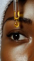 Golden oil drop falling near brown eye with long lashes, close-up beauty shot showing skincare and cosmetic treatment application on dark skin.