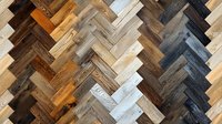 Rustic wooden parquet flooring in herringbone pattern showcasing various wood tones from dark charcoal to whitewashed planks, creating dynamic geometric design.