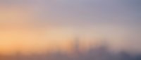 Blurred urban skyline at sunrise with soft golden and purple tones, suitable for backgrounds, web design, and atmospheric overlays.
