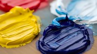 Colorful acrylic paint palette with yellow blue red white pigments mixed on wooden surface for artistic creative projects and painting techniques.