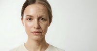 Young woman face showing aging process with wrinkles and skin changes on neutral background for skincare and beauty treatment concepts.