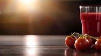 Fresh tomato juice in tall glass with ripe red tomatoes on rustic wooden table against dark background with copy space. Natural healthy beverage concept.