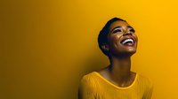 Young African American woman with short hair wearing yellow sweater laughing joyfully against vibrant yellow background, expressing genuine happiness and positive emotions.