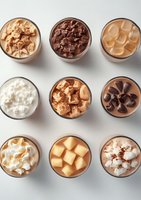 Variety of cold coffee drinks with different toppings and mix-ins viewed from above on light background, including iced lattes, mochas, and cream-topped beverages.