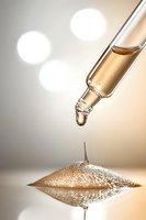 Glass dropper with golden serum creating mirror reflection on glossy surface against soft bokeh background, capturing moment before drop falls in macro photography.