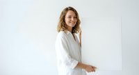 Young blonde female doctor in white medical coat smiling confidently against clean white background for healthcare and medical professional concepts.
