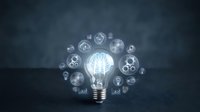 Glowing light bulb with brain inside surrounded by floating business and technology icons on dark background representing innovation and creative thinking.
