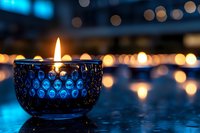 Glowing blue glass candle holder with burning flame against dark background, creating magical bokeh light effect. Atmospheric evening mood for spa and wellness.