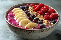 Vibrant smoothie bowl with dragon fruit, banana slices, fresh raspberries, blueberries, granola and chia seeds arranged in colorful rows for healthy breakfast.