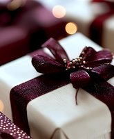 Elegant white gift box with burgundy ribbon bow and golden beads, festive holiday present with warm bokeh lights background for celebrations and special occasions.