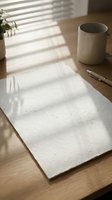 Blank paper sheet on wooden desk with ceramic mug and pen, natural window light creating shadows for writing, journaling or creative work.