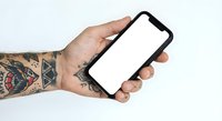Tattooed hand holding smartphone with blank white screen mockup for app presentation and mobile interface design on white background.