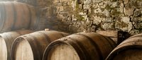 Wooden barrels stacked in a rustic winery cellar with aged stone walls, suitable for wine production, beverage industry, and vineyard marketing materials.