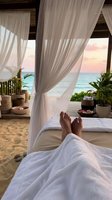Relaxing on luxury beach bed with flowing white curtains, ocean view, and tropical plants at sunset resort spa.
