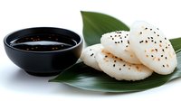 Asian rice cakes with black sesame seeds served on banana leaf with soy sauce for traditional Japanese Korean cuisine cooking ingredients.