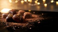Chocolate truffles dusted with cocoa powder arranged on dark surface with warm bokeh lights, suitable for bakery, confectionery, and food advertising projects.