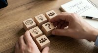 Business strategy planning with wooden blocks featuring lightbulb, team and question mark icons on desk with notebook and pen for corporate decision making.