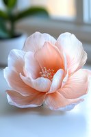 Delicate peach-colored paper flower with intricate petals and stamens on soft white background, showcasing detailed craftsmanship and gentle natural lighting.