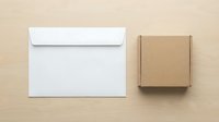 White envelope and brown cardboard box on beige background for shipping and mailing business correspondence mockup flat lay composition.
