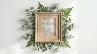 Wooden frame surrounded by fresh green ferns and eucalyptus leaves on white background, suitable for home decor, botanical design, and nature-themed projects.