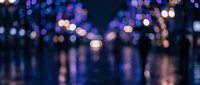 Abstract blurred city lights bokeh background with purple and blue tones reflecting on wet surface creating dreamy atmospheric nighttime scene.
