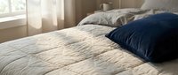 Cozy bedroom interior with neatly arranged pillows on a quilted bed, featuring soft natural light from window and warm neutral tones for home decor and lifestyle content.