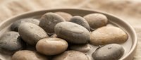 Smooth river stones arranged in wooden bowl on natural textile background for spa wellness meditation and zen relaxation concepts.